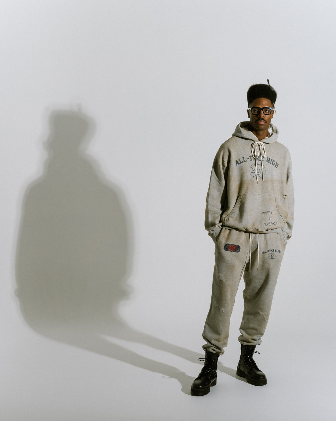  Mark wearing all time high cotton fleece heather grey graphic sweatpants and hoodie standing on white studio backdrop with shadow silhouette