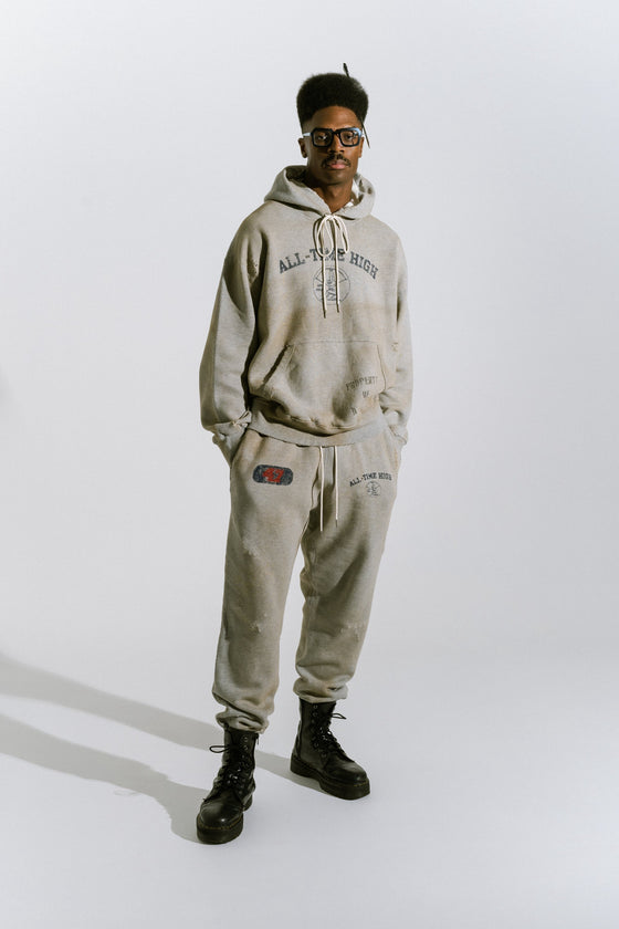 Model in photo studio wearing heather grey cotton fleece graphic hoodie with matching graphic sweatpants and black leather boots