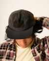 Person wearing a black cap and a patterned jacket on a plain background