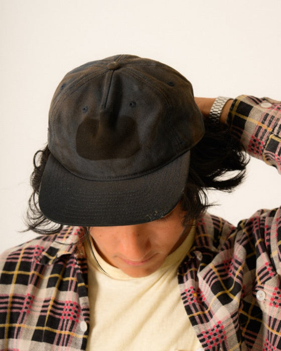 Person wearing a black cap and a patterned jacket on a plain background