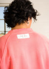 Person wearing a pink sweatshirt with a brand label, facing away from the camera.