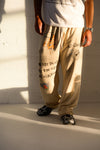Person wearing beige pants with text and graphics, standing against a light-colored wall.