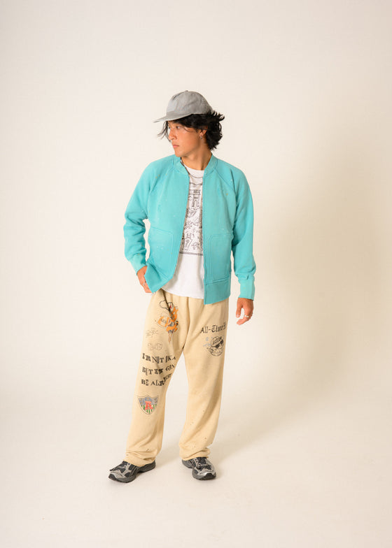 model wearing turquoise blue zip up sweatshirt and gray hat facing left in studio
