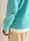 Teal hoodie with distressing on the sleeve against a neutral background
