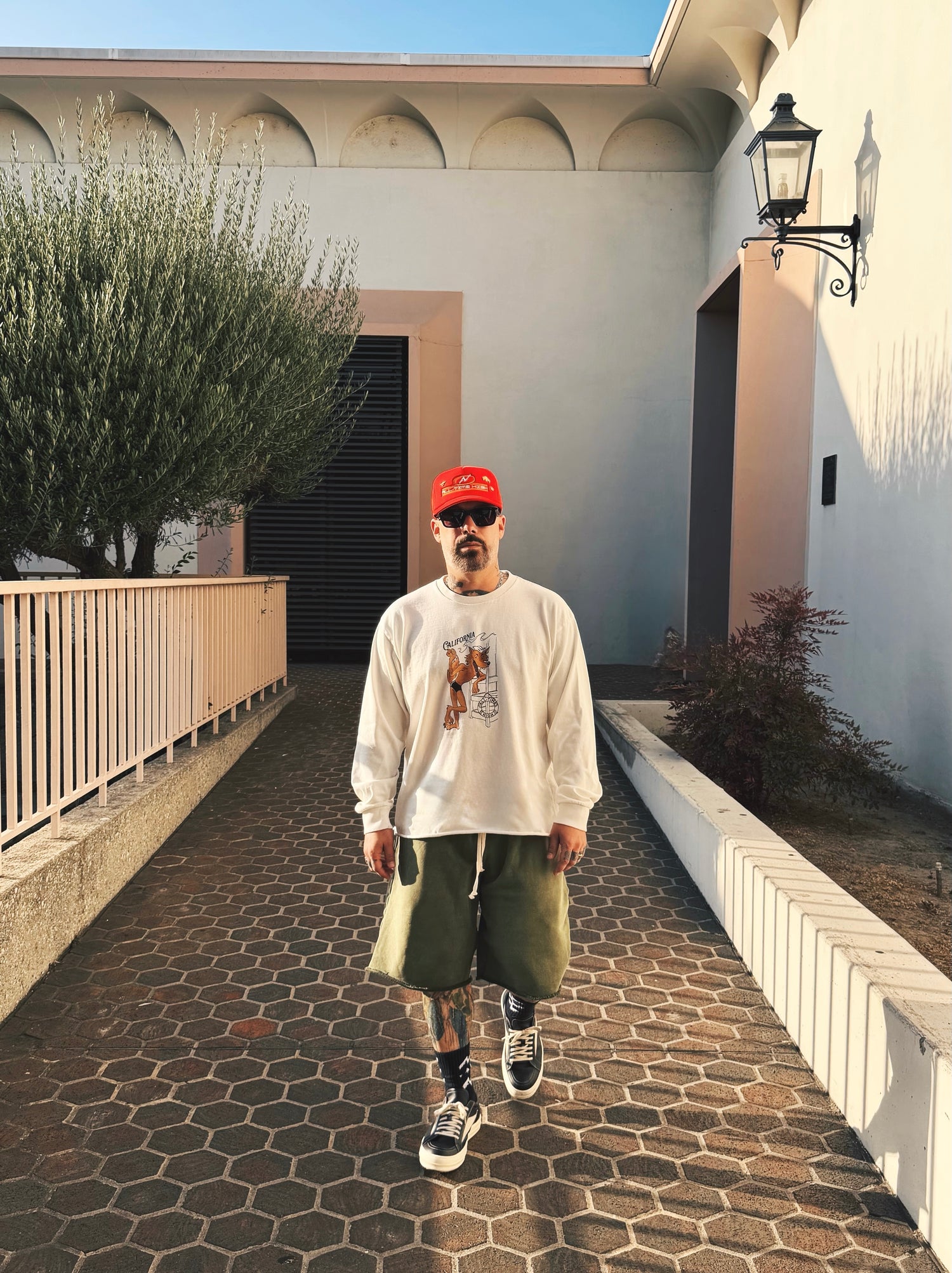 Man in front of mid century building in red trucker hat, long sleeve shirt and green shorts