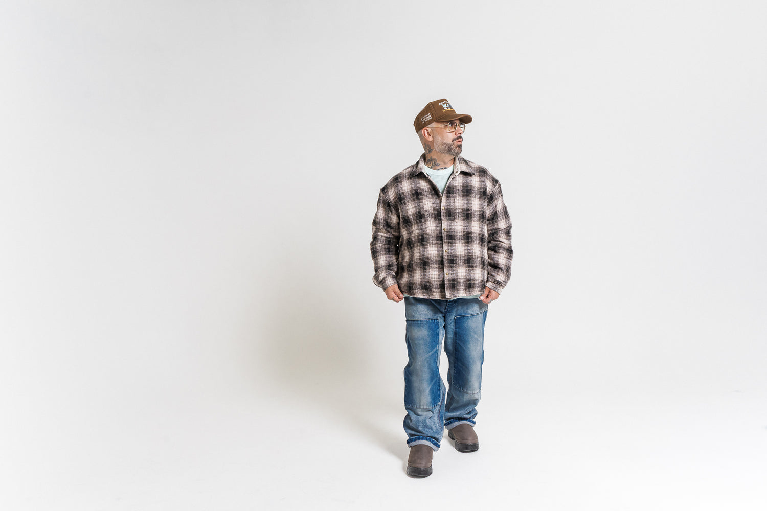 Man wearing a plaid shirt and jeans standing against a white background