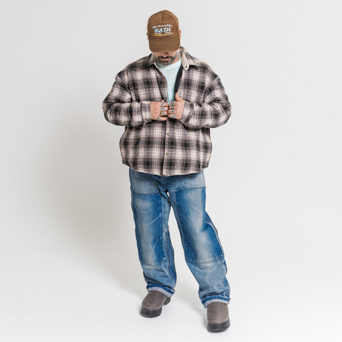 Man wearing a plaid shirt, jeans, and a cap on a white background